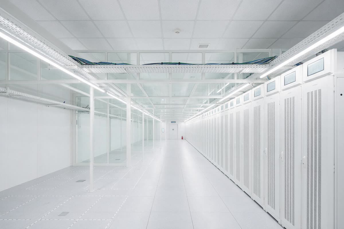 A bright data centre aisle with cabinets installed along one side and bare floor tiles marked out for the next positions on the other.