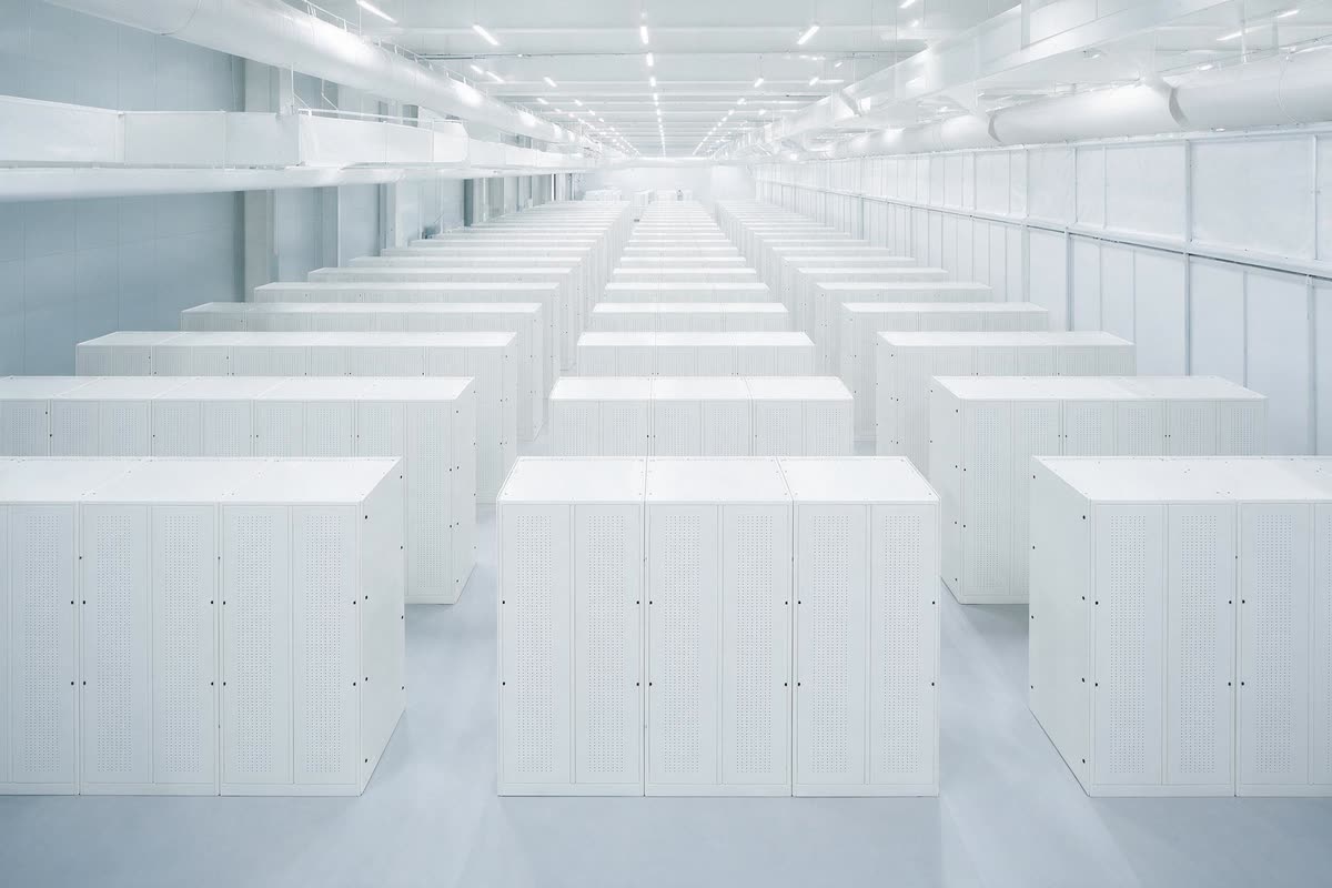 A wide view over many parallel rows of white server cabinets filling a large bright data hall.