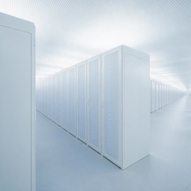 A lit aisle of GPU compute racks in a white data hall, cabinet doors closed and status lights running the length of the row.